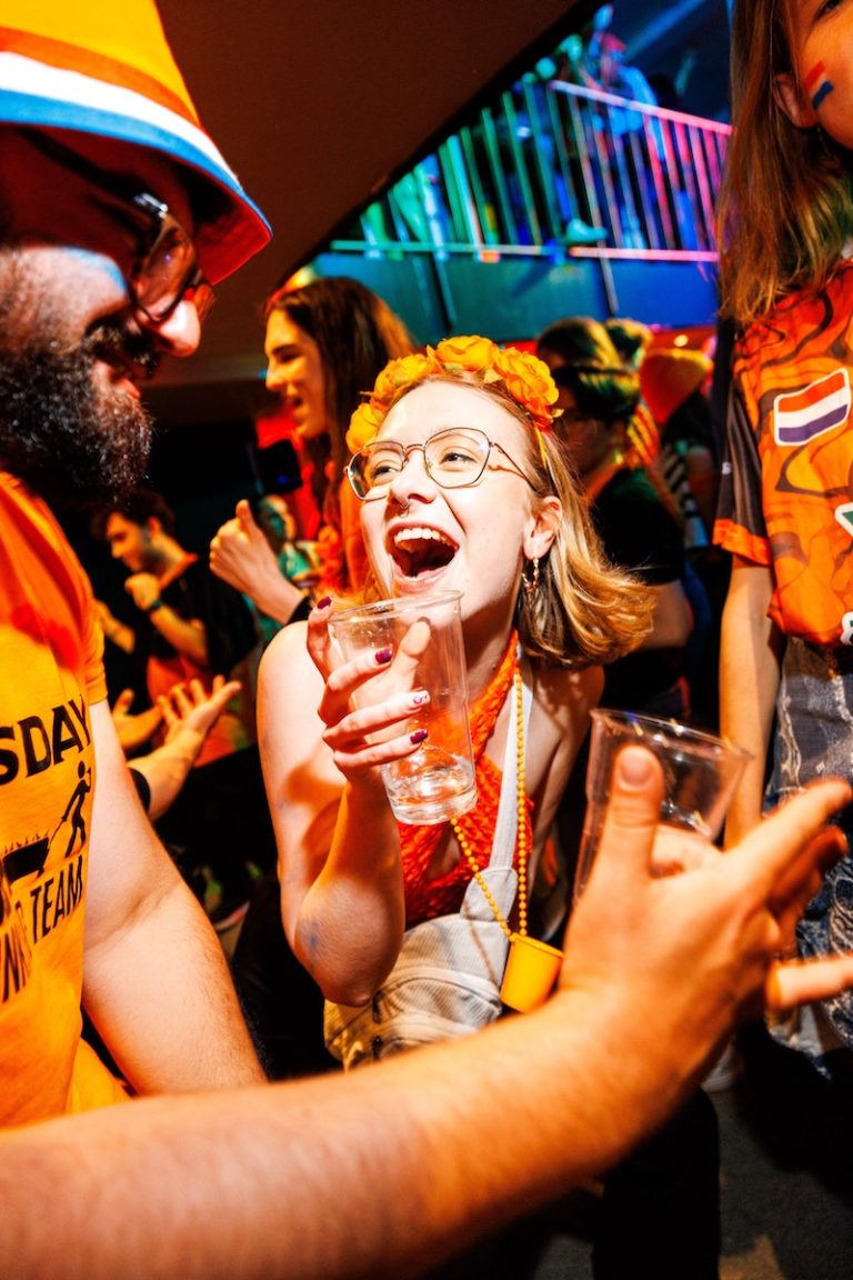 Group of travelers laughing and holding drinks while celebrating King’s Day in Amsterdam.