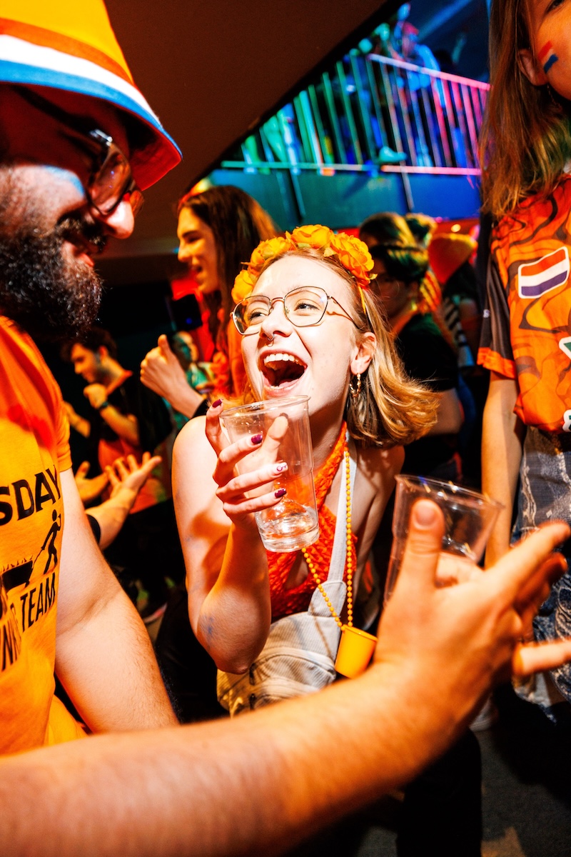 Group of travelers laughing and holding drinks while celebrating King’s Day in Amsterdam.