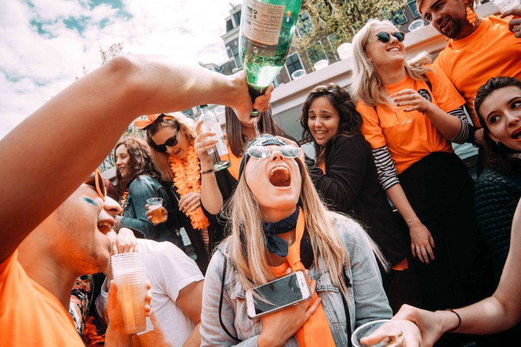 Young travelers enjoying a lively Kings Day Koningsdag party in Amsterdam, wearing orange and celebrating during the citywide festival.