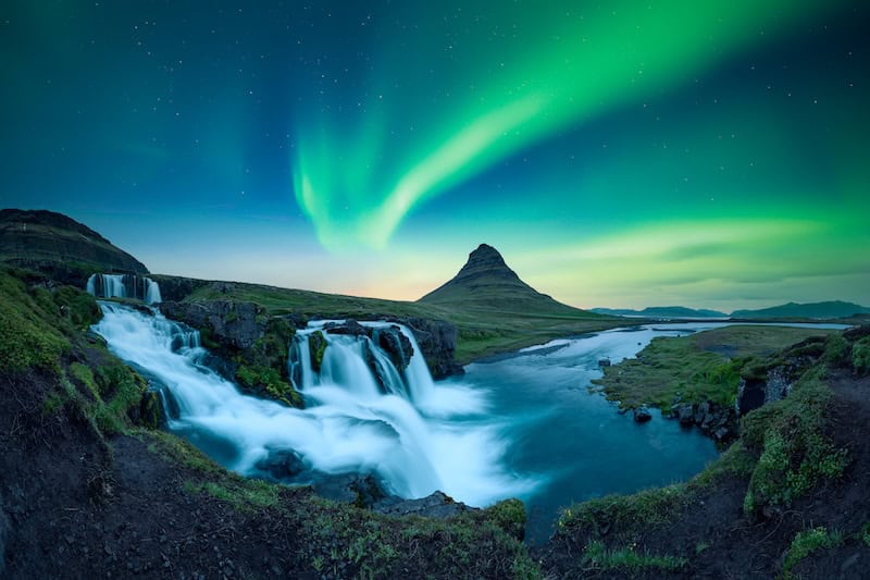 Northern lights glowing above Kirkjufellsfoss waterfall and Mount Kirkjufell in Iceland