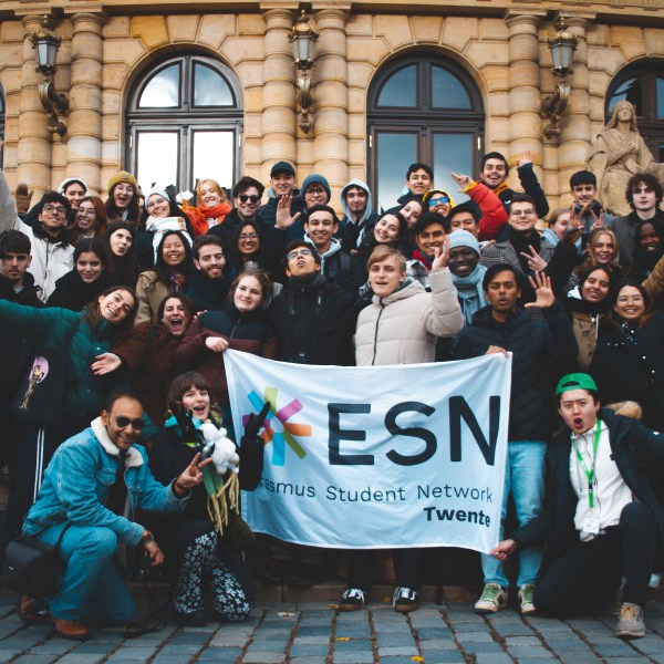 Group of students holding an ESN Twente banner in front of a building.