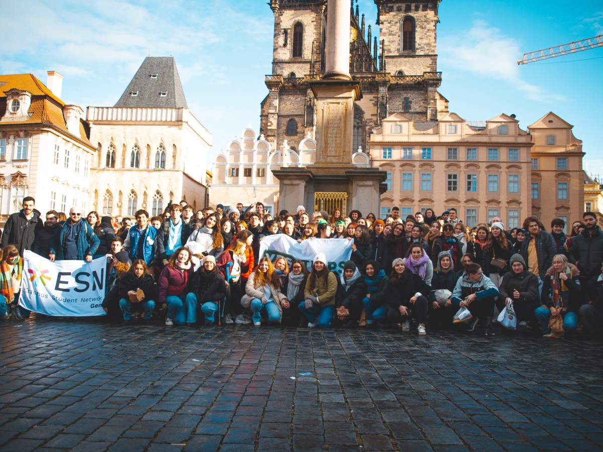 Large group photo in historic city square with banner and old buildings.