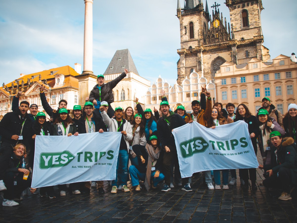 Group of people holding 'Yes-Trips' banners in a historic city square.