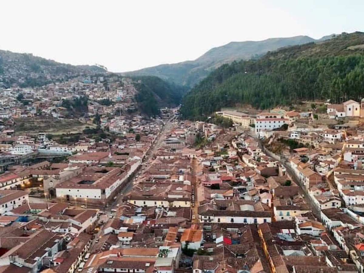 Aerial view of a town with red-tiled roofs, surrounded by mountains.