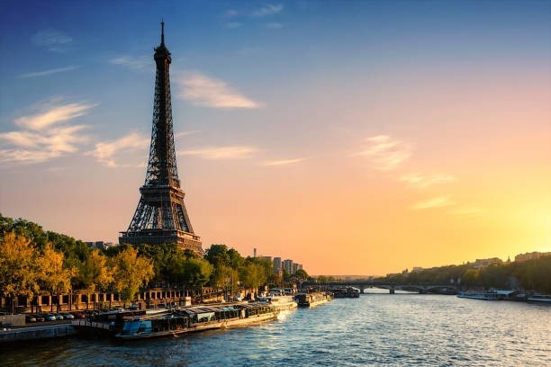 Eiffel Tower by the Seine River at sunset with trees and boats.