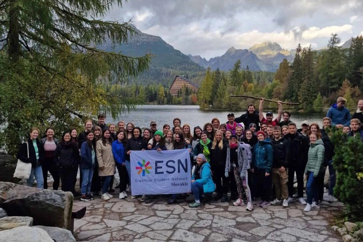 Group of people with 'ESN' banner by a lake and mountains.
