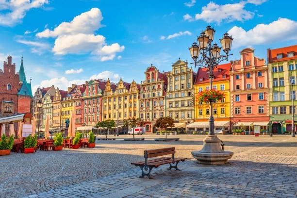 Colorful historical buildings line a cobblestone square under a blue sky with clouds.