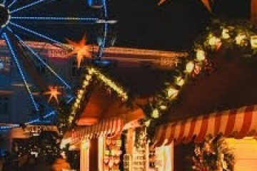 Festive market with lights and Ferris wheel at night.