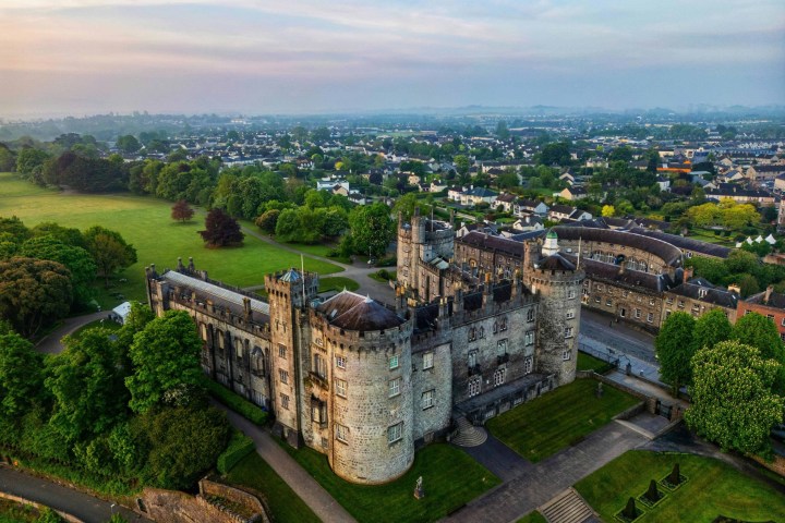 Aerial view of a historic stone castle surrounded by greenery and distant town.
