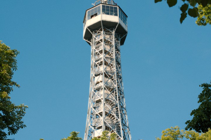 Tall, lattice tower with an observation deck framed by green trees against a clear blue sky.