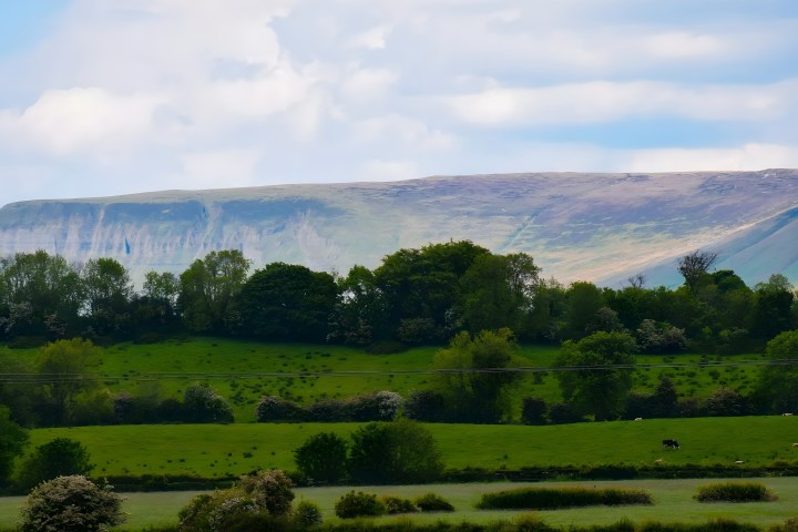 Rolling green fields with distant hills under a cloudy sky.