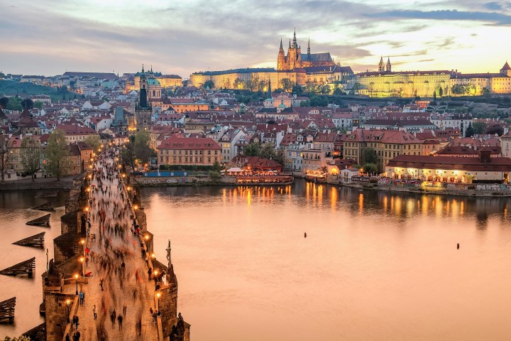 View of a historic bridge and illuminated castle at sunset over a river.