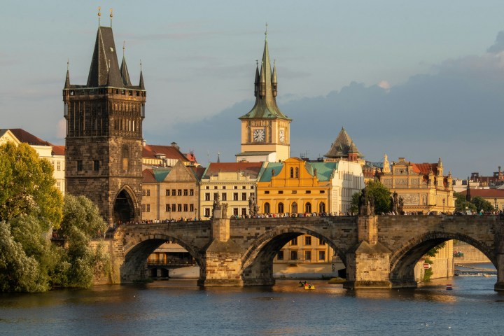 Historic stone bridge with towers and city buildings at sunset.
