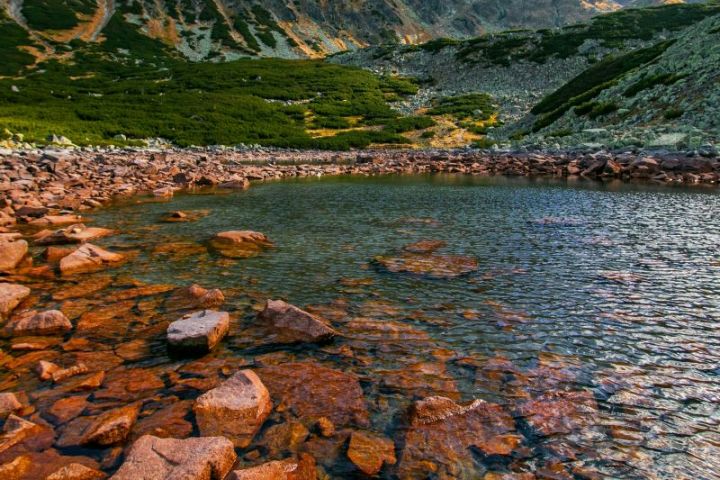 Mountain lake with rocky shore under a clear blue sky.