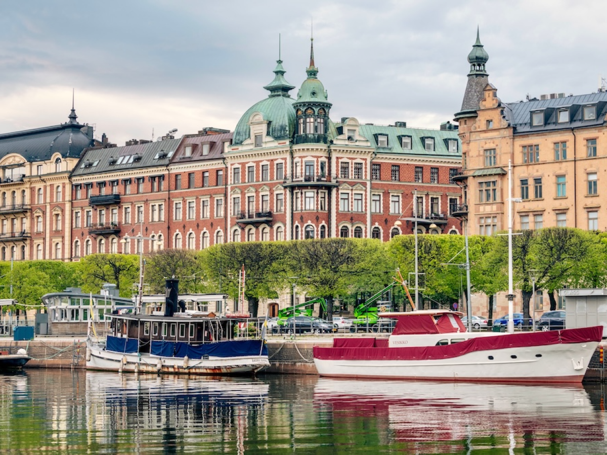 Boats docked by ornate, historic buildings in a waterfront cityscape.