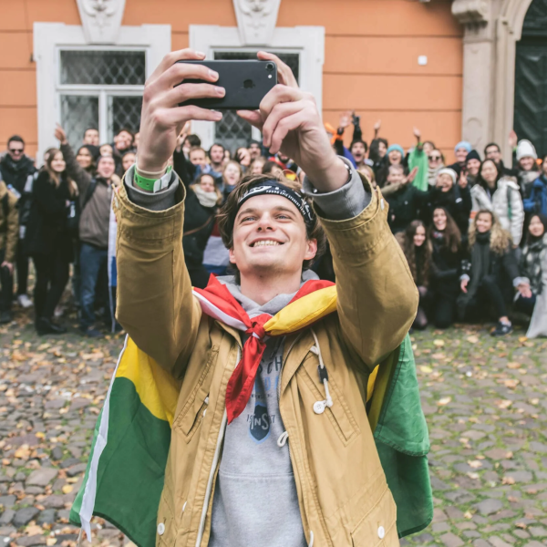 Group of people pose for a selfie with a man in the foreground holding a smartphone.