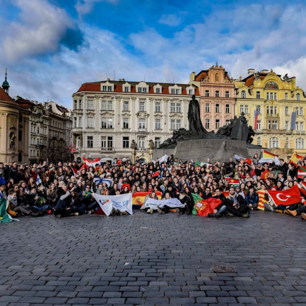 Large group with flags in a historic square with colorful buildings.