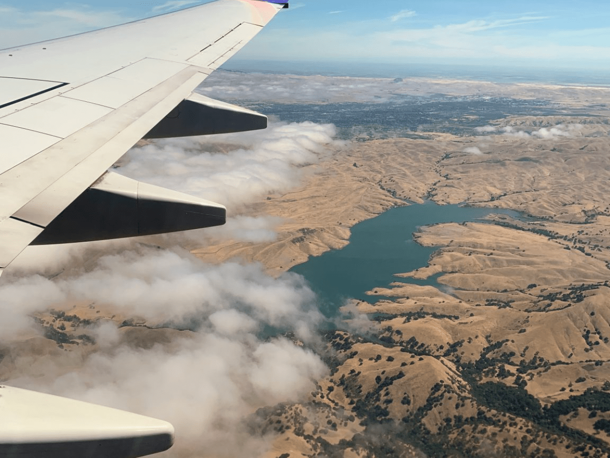 View from airplane wing over landscape with river, hills, and clouds.