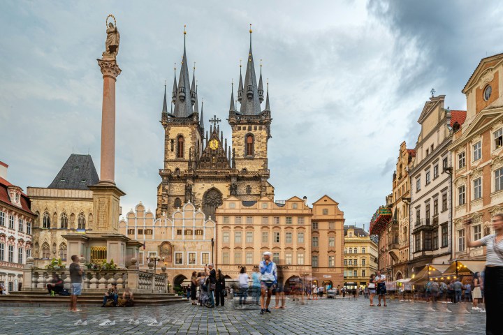 Historic city square with a Gothic church and column under a cloudy sky.
