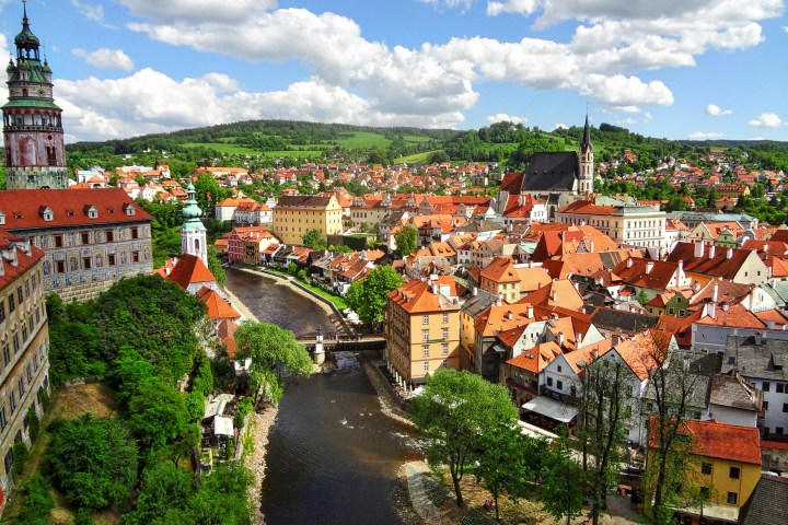 Aerial view of a historic European town with red roofs, a river, greenery, and a church.