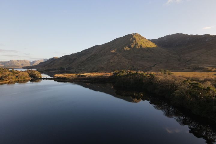 Serene lake reflecting a mountain under clear sky at sunset.