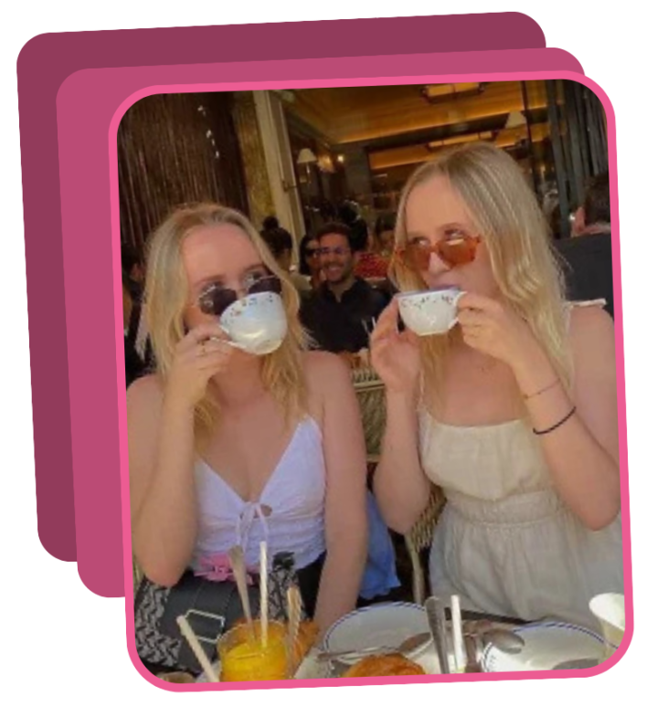 Two people sitting outdoors, sipping drinks from cups.