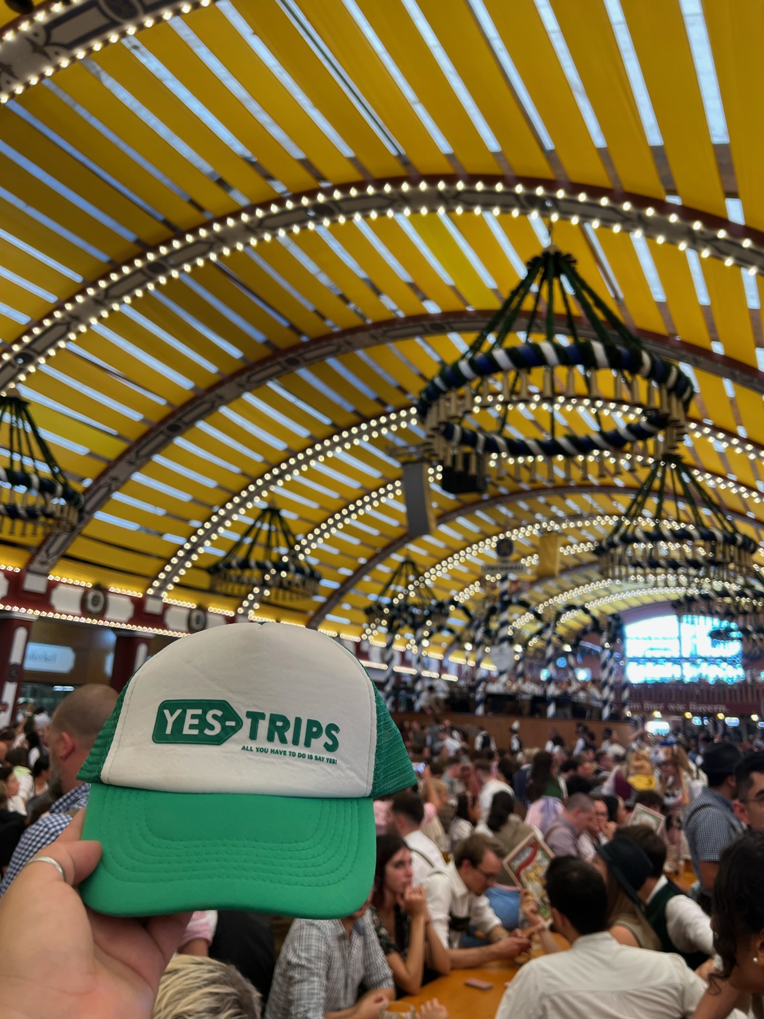 Crowd under a yellow-striped canopy holds up YES-TRIPS cap