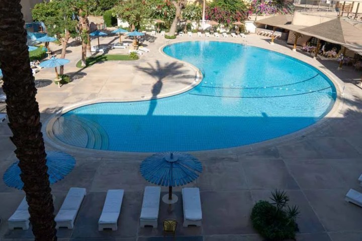 Aerial view of a bean-shaped swimming pool with lounge chairs and umbrellas on a sunny day.