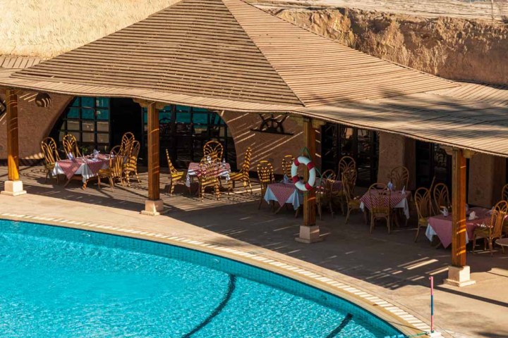 Outdoor café with tables by a large blue swimming pool.