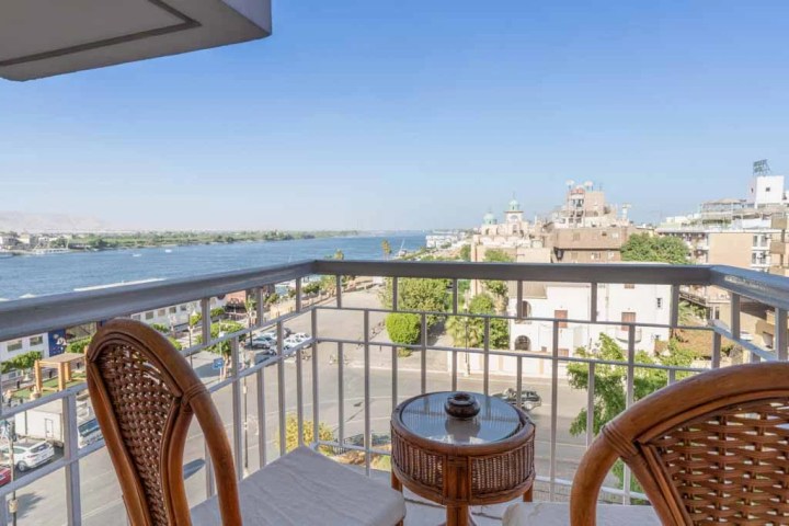 Balcony view of river and cityscape with two chairs and a small table.