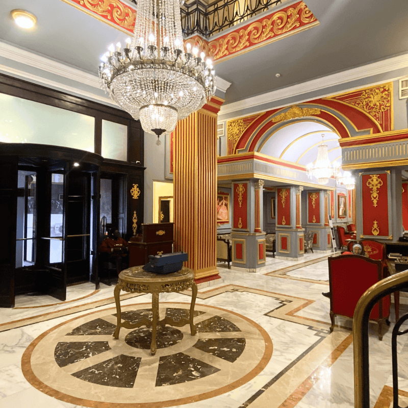 Luxurious hotel lobby with ornate decor, chandeliers, and a revolving door.