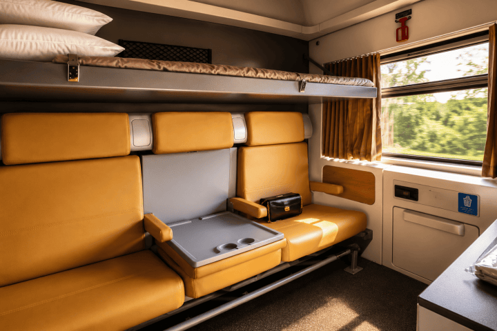 Train cabin with yellow seats, a fold-down table, and a window with curtains.