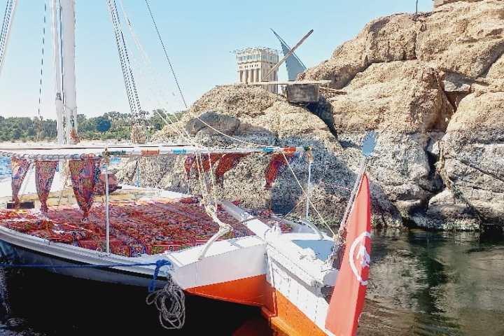 Boat docked at rocky shore with windmill and historical building in the background.
