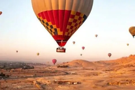 Hot air balloons float over a desert landscape at sunrise.