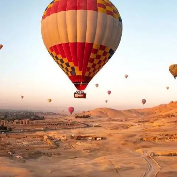 Hot air balloons float over a desert landscape at sunrise.