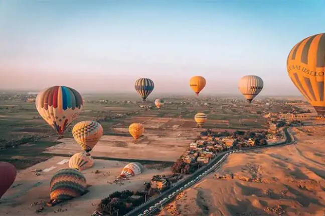 Hot air balloons floating over a desert landscape at sunrise.
