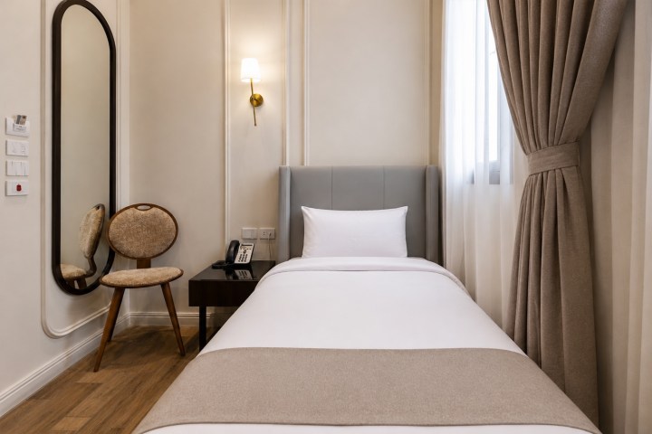 Cozy hotel room with a single bed, chair, wall lamp, and window with curtains.