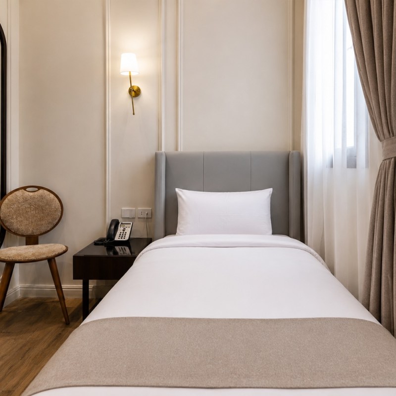 Cozy hotel room with a single bed, chair, wall lamp, and window with curtains.