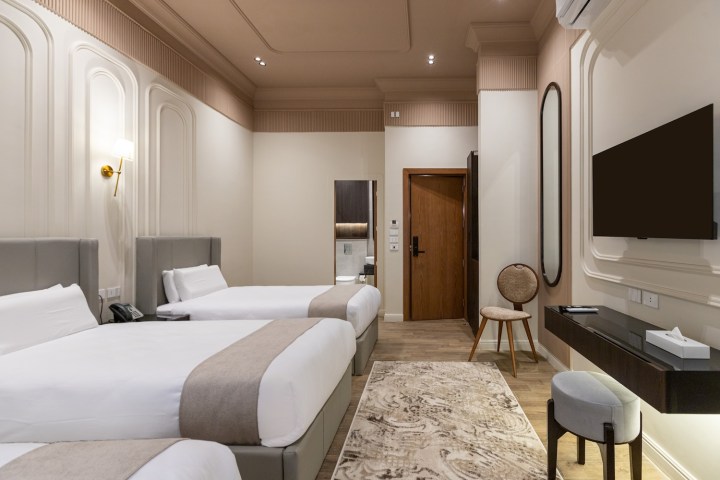 Modern hotel room with two beds, TV, desk, chair, and beige decor.