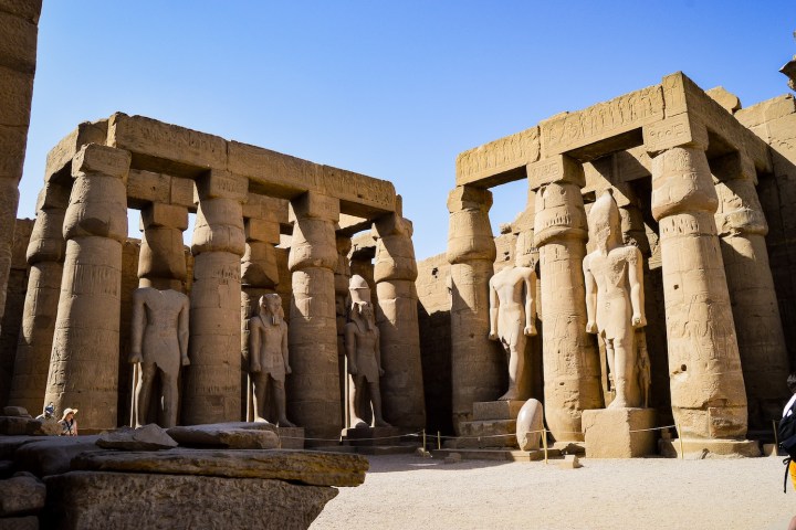 Ancient stone ruins with statues and columns under a clear blue sky.