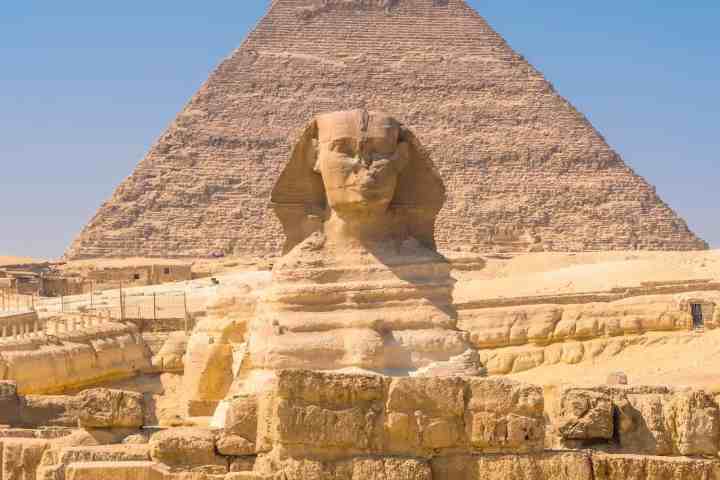 Sphinx in front of a pyramid under a clear blue sky.