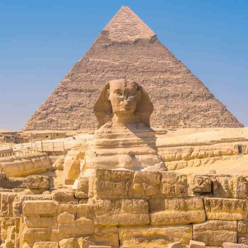 Sphinx in front of a pyramid under a clear blue sky.