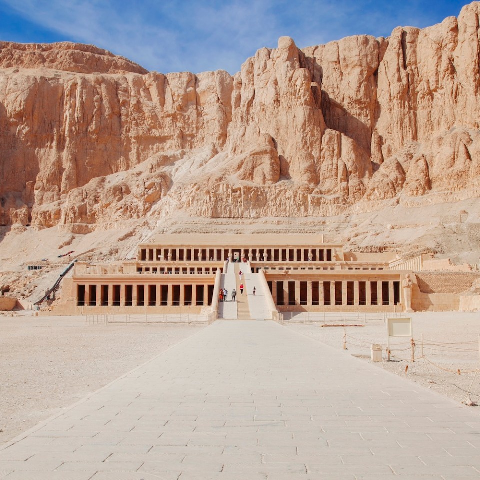 Ancient temple built into rocky cliffs under a blue sky.