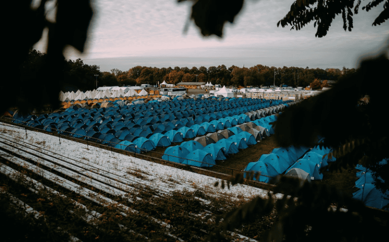 Aerial view of a large field filled with rows of blue tents under a cloudy sky.