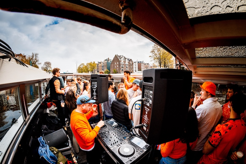 People partying on a boat with a DJ and speakers, outdoor scene.